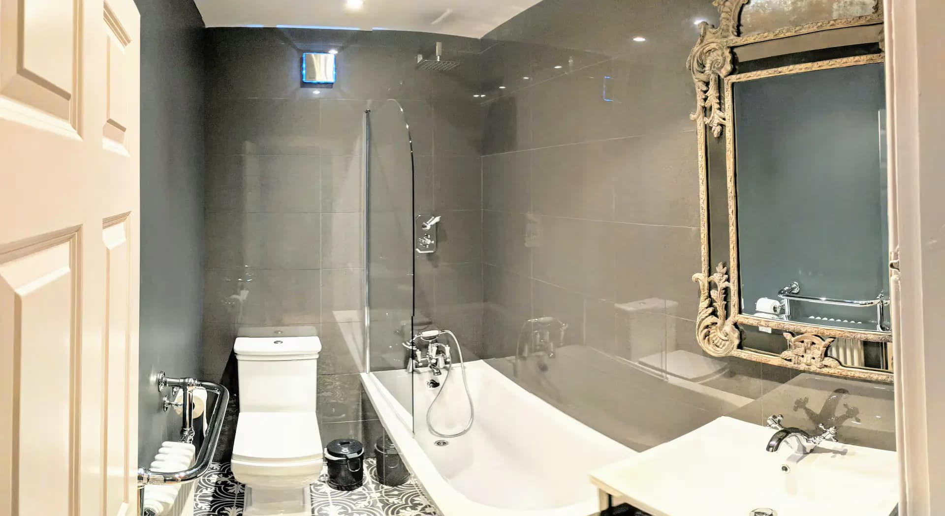 Bathroom with bath, shower screen and dark tiled walls inside Luxurious Home.