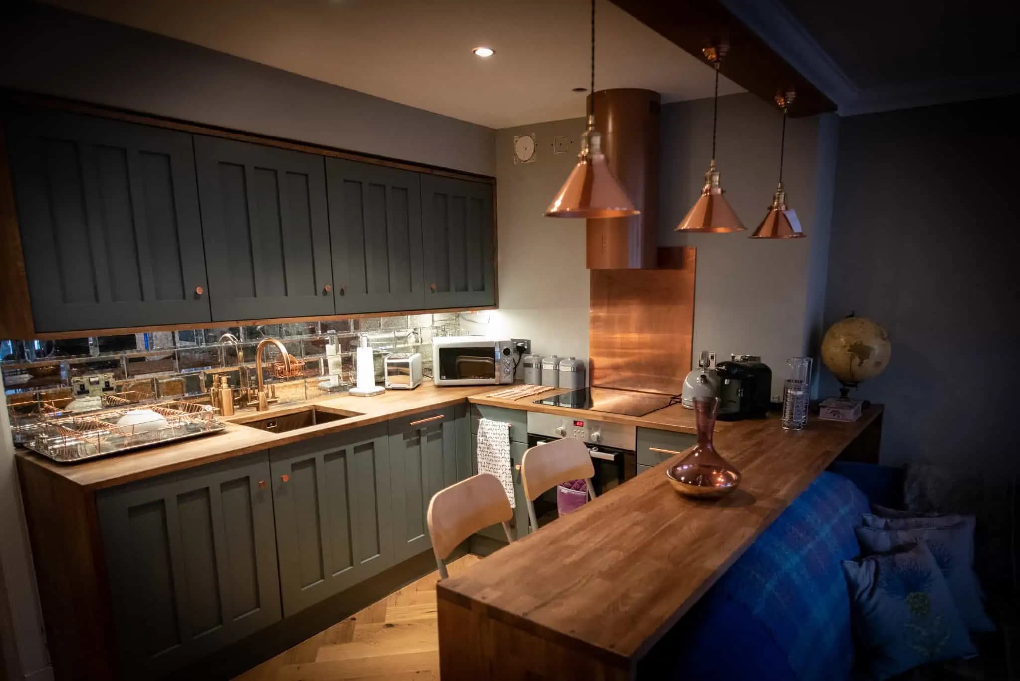 Dark fitted kitchen with copper pendant lights inside Luxurious Home.